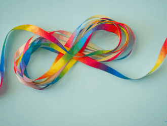 A colorful rainbow ribbon arranged in the shape of an infinity symbol on a light blue background, representing autism awareness and neurodiversity.