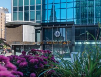Exterior of the UConn School of Business building in downtown Hartford with reflection of the city skyline and flowers in the foreground.
