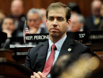 A man in a suit seated in a legislative chamber