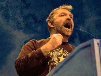A speaker at a podium raising a fist while addressing a crowd.